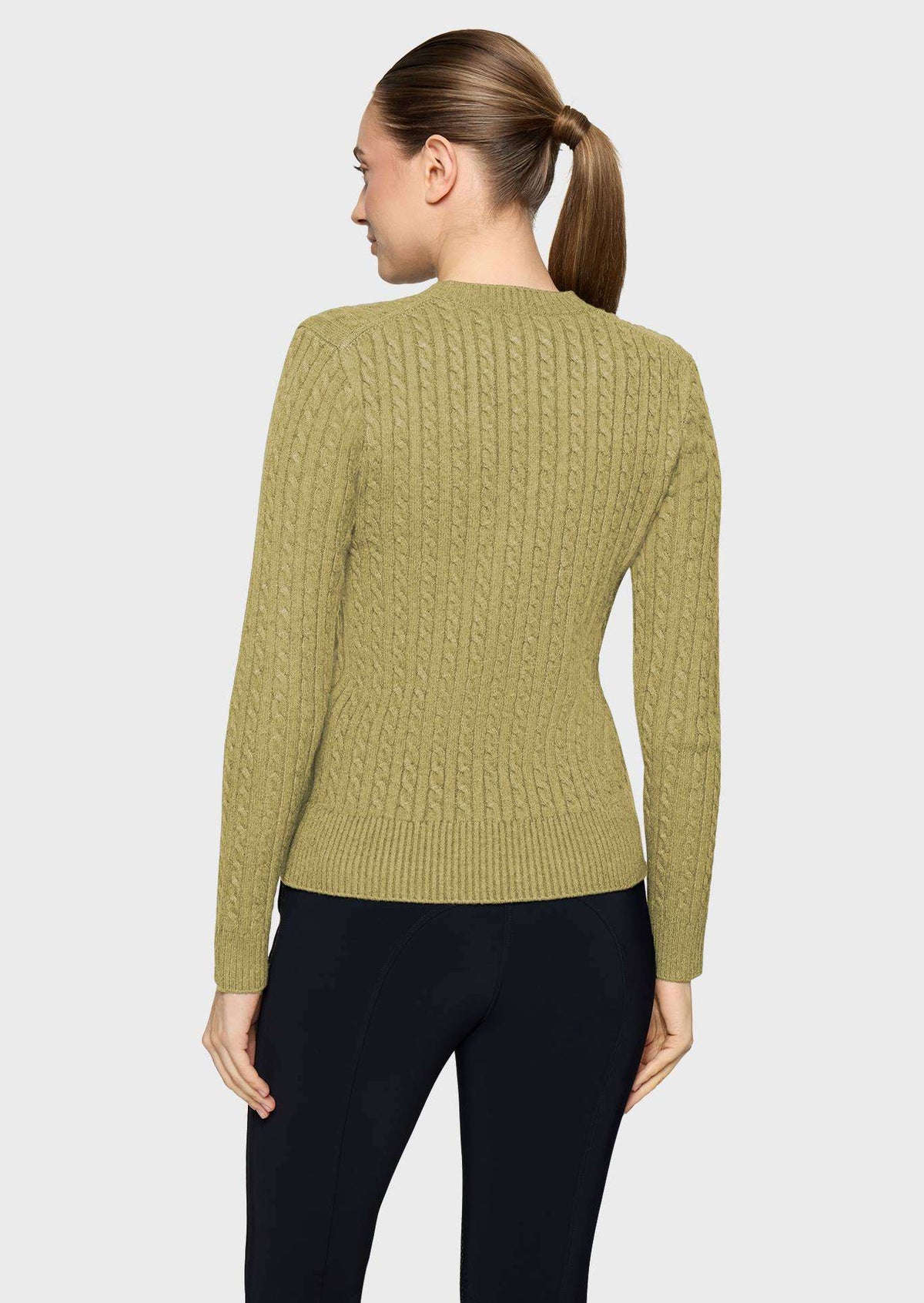 A woman shown from the back wearing a fitted cable-knit sweater in a muted olive green color, paired with black pants, against a light gray studio background.