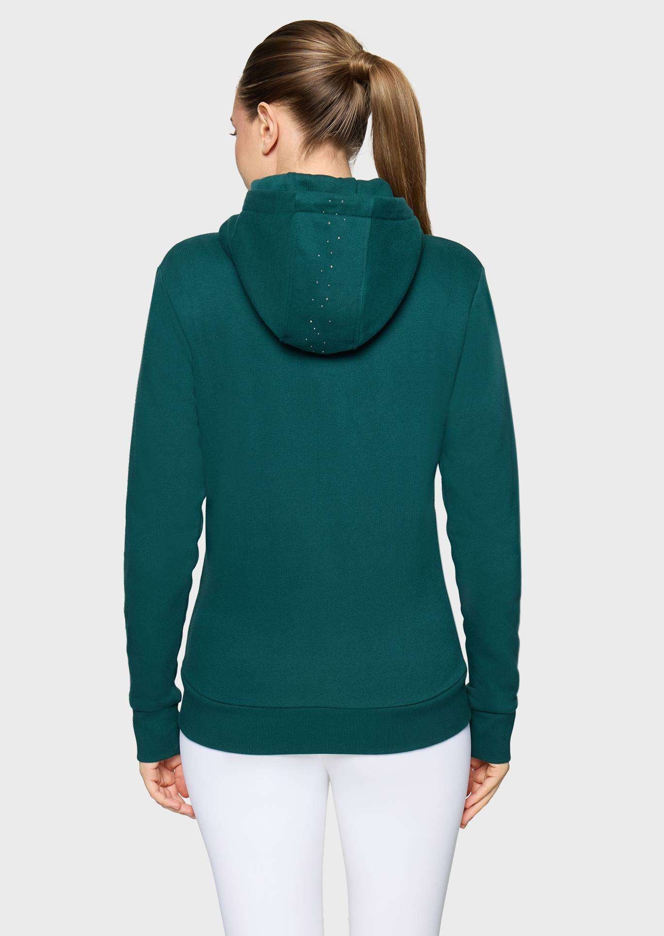 A woman viewed from the back wearing a dark teal-green long-sleeve hoodie and white leggings against a light gray studio background.