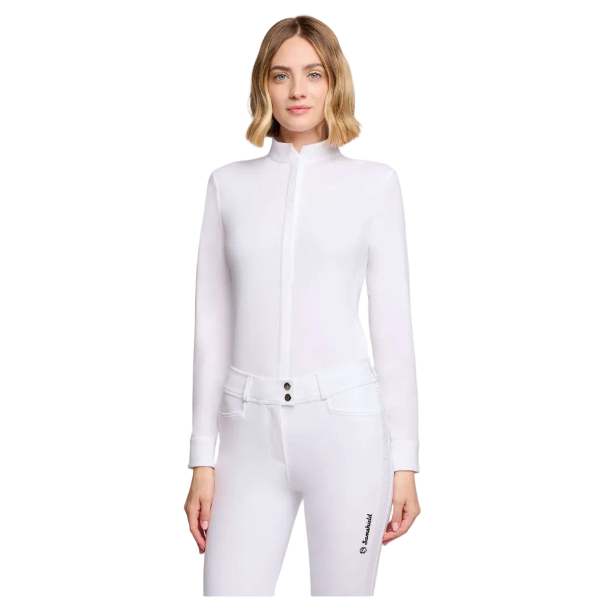 A woman modeling a white long-sleeve equestrian-style jacket with a high mock neck and front zipper, paired with matching white riding pants, against a light gray studio background.