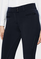 Close-up of a person wearing dark navy equestrian riding breeches, showing the front waistband with two buttons, side zip pocket, and leg stitching details.