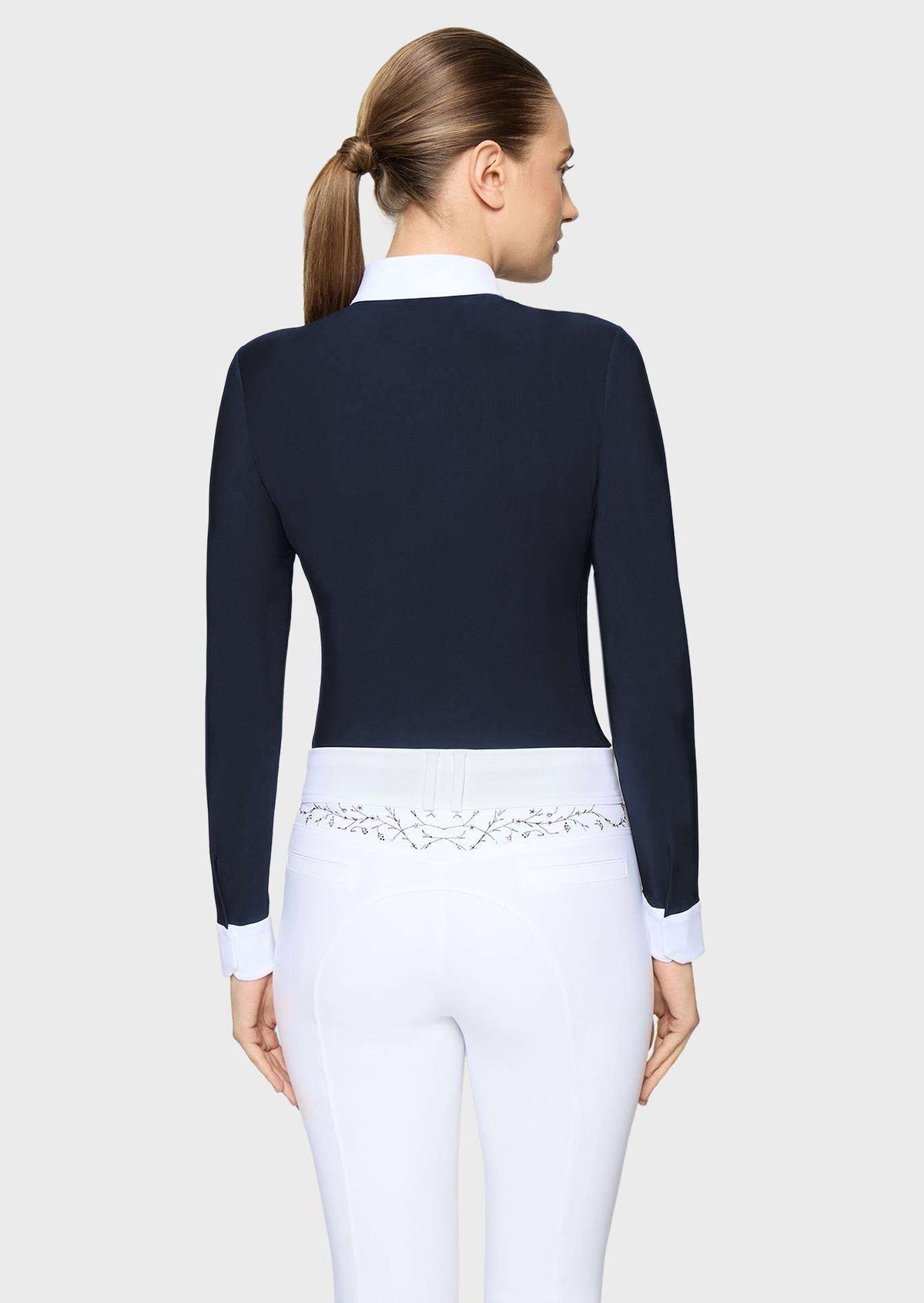 A woman shown from the back wearing a fitted dark navy long-sleeve top with a white collar and white cuffs, paired with white pants featuring a decorative embroidered waistband.