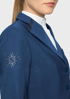Close-up of a woman wearing a navy blue blazer with a white high-neck shirt underneath. The blazer features a decorative silver crystal pattern on the left sleeve and a black beaded trim detail on the collar.
