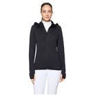 A woman modeling a black hooded zip-up athletic jacket over a white top and white pants, photographed against a light gray studio background.