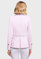 A woman shown from the back wearing a light pink tailored blazer with a peplum waist and a sparkly silver embellishment at the center, paired with white pants against a light gray studio background.