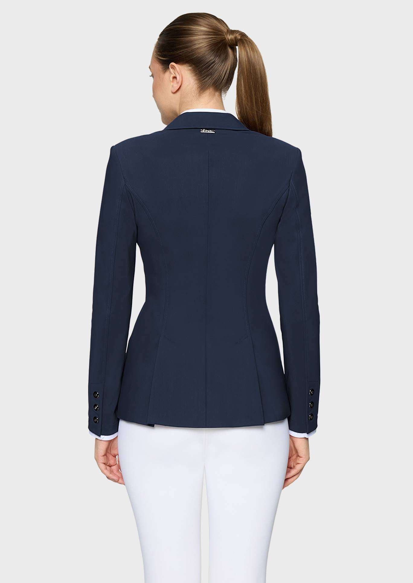 A woman shown from the back wearing a navy blue tailored blazer and white trousers against a light gray studio background.