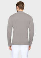 A man viewed from the back wearing a light gray ribbed knit sweater and white trousers, standing against a plain light gray studio background.