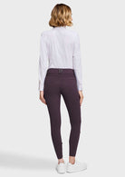 A woman is shown from the back wearing a white long-sleeve blouse and dark plum ribbed leggings, paired with white sneakers, against a light gray studio background.