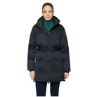 A woman modeling a black hooded puffer coat with a matching belt, worn over a green turtleneck sweater, against a light gray studio background.