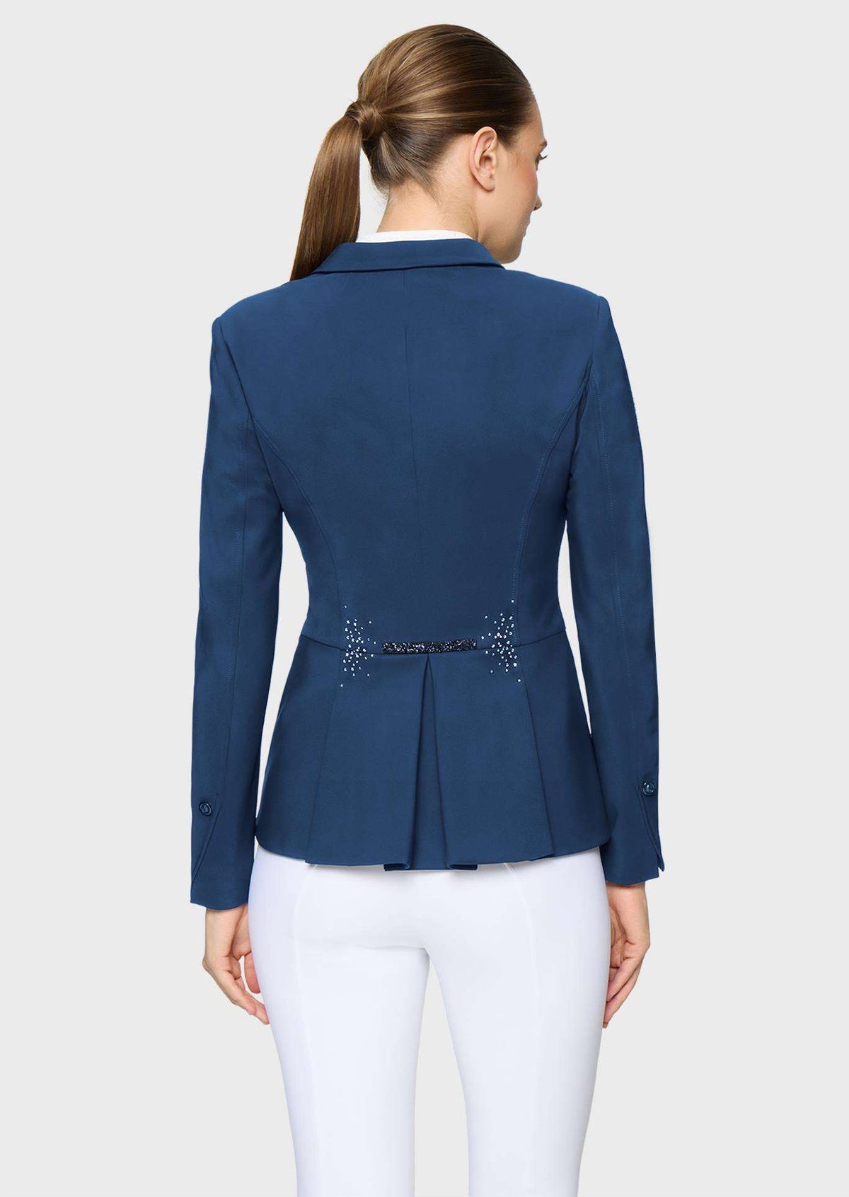 A woman shown from the back wearing a navy blue tailored blazer with a peplum-like waist and small embellished detail at the center back, paired with white pants, against a light gray studio background.