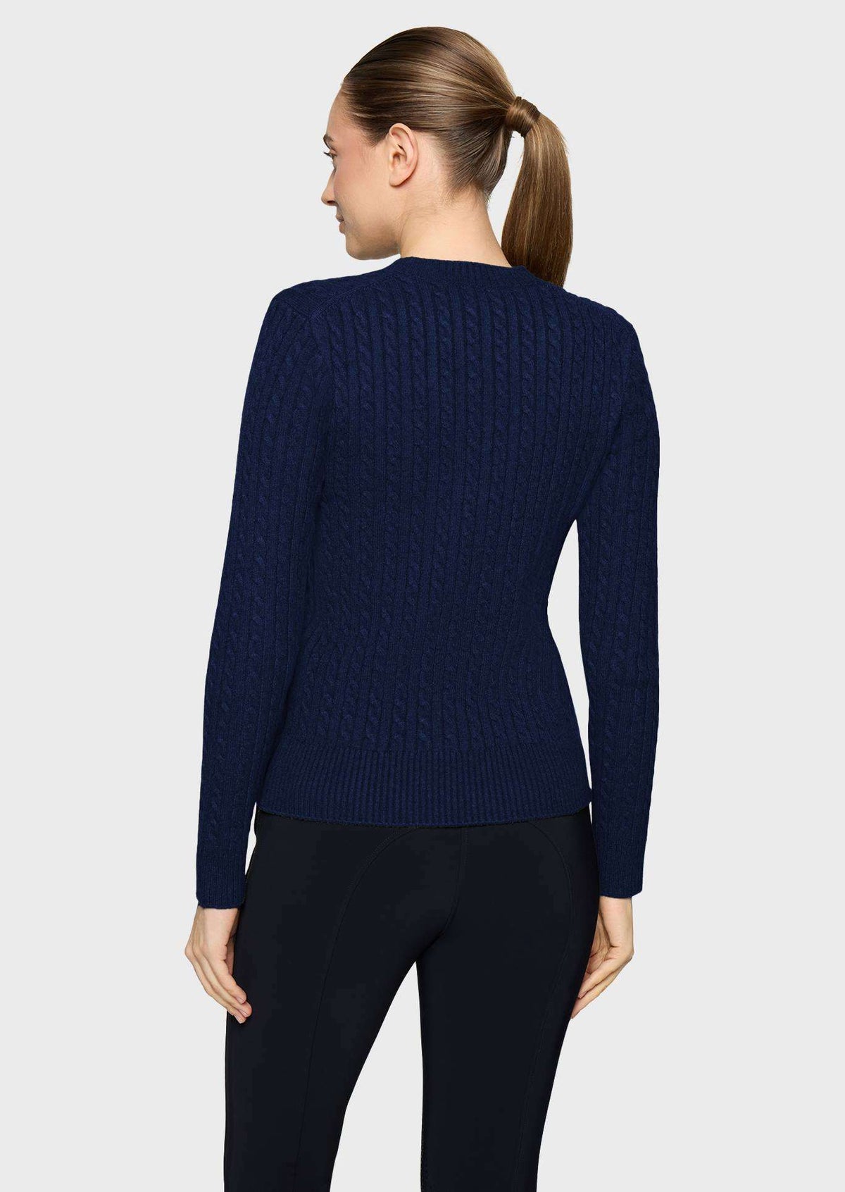 A woman shown from the back wearing a navy blue cable-knit sweater and black leggings against a light gray studio background.