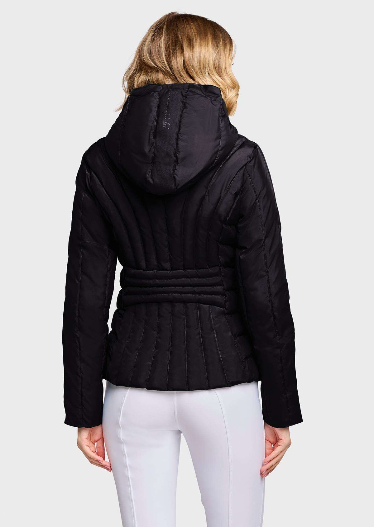 A woman shown from the back wearing a black quilted hooded jacket with a belted waist and white pants, against a light gray studio background.