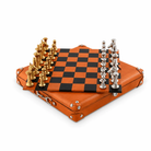 A gold and silver chess set on an amber and black chequered board, sitting on a amber case featuring silver hardware. 