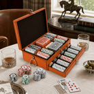 An orange leather poker chip storage case with multiple compartments and two open drawers, filled with stacks of poker chips in red, green, black, and white. The case is styled on a table with playing cards, glasses of whiskey, olives, and a horse statue in the background.