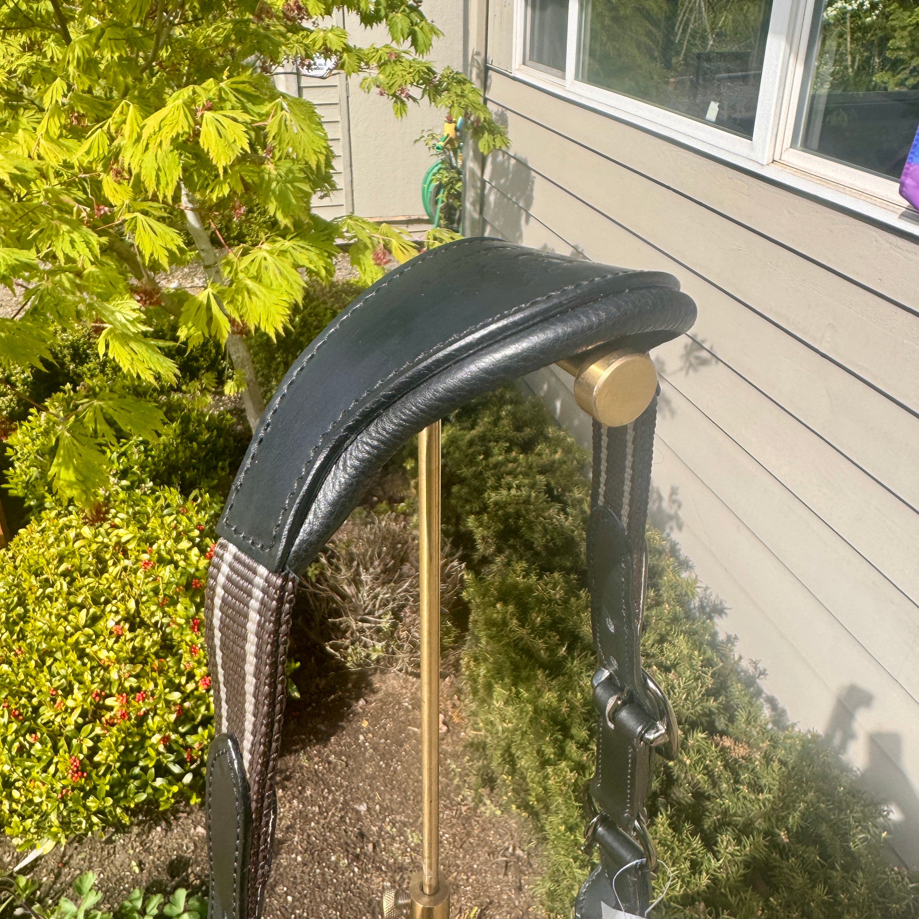 Black leather archery bow grip with gold accent on a stand outdoors.