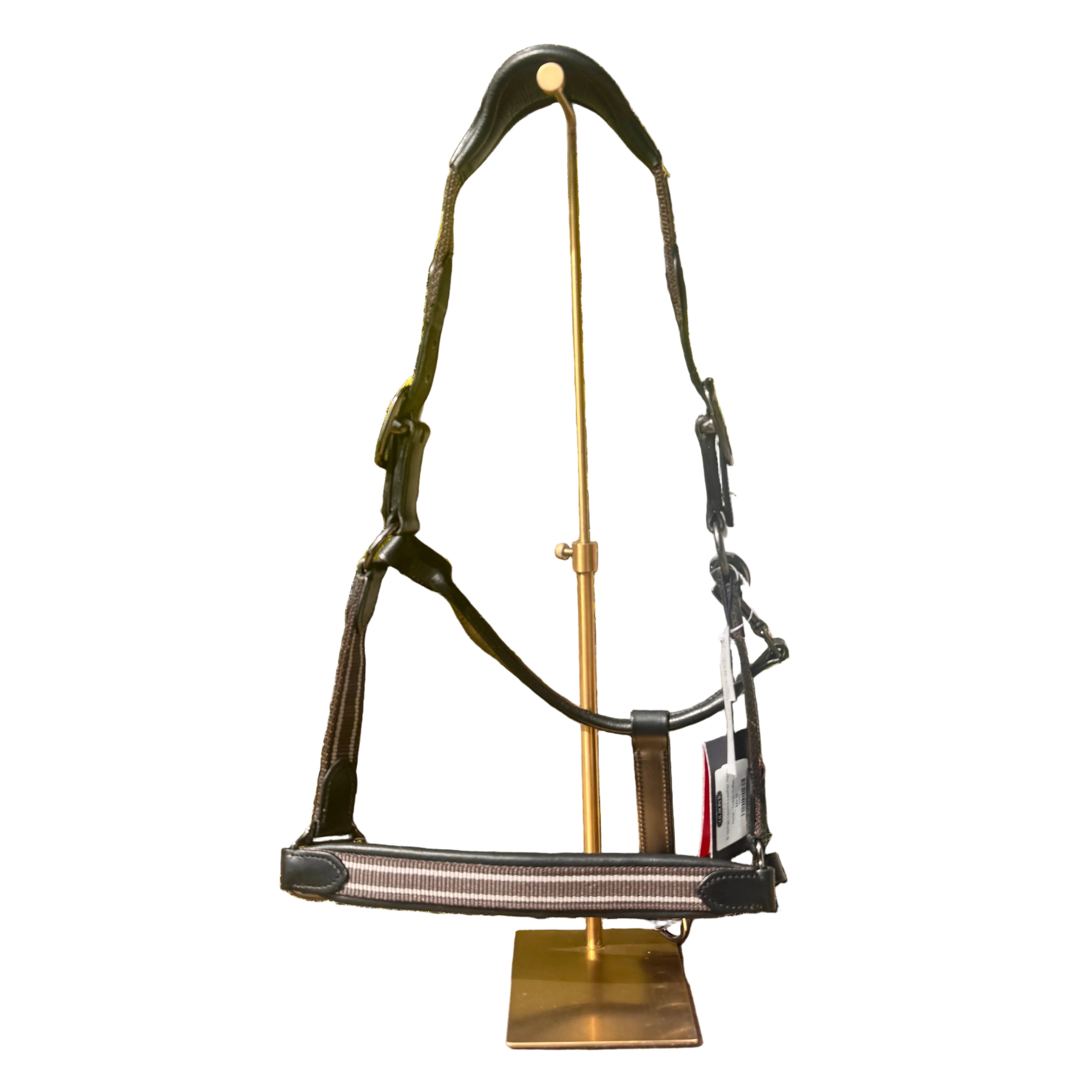 Decorative metal horse bridle on a stand outdoors with trees and a house in the background