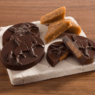 Chocolate candies with horse designs on a stone platter with caramel pieces on a wooden surface