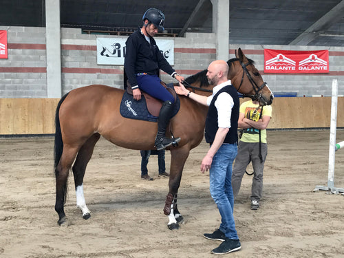 Person on horseback with two others assisting in an indoor arena.
