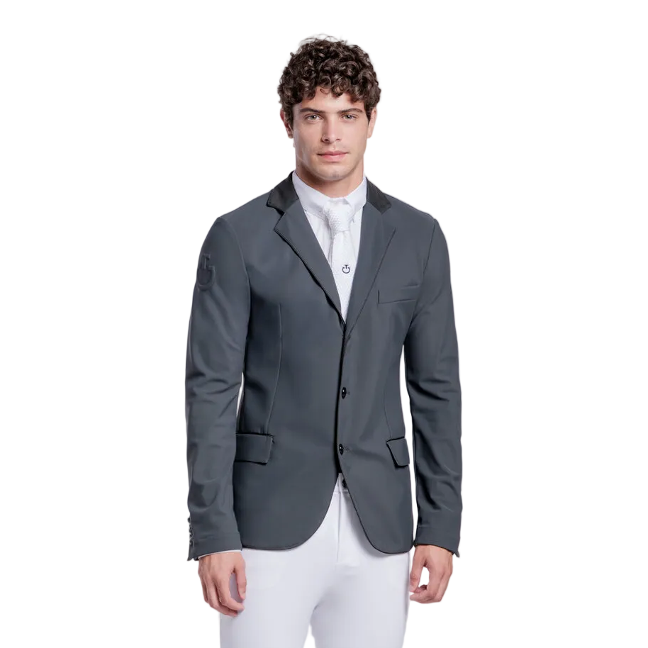 A man modeling a dark gray equestrian sport coat, white breeches, and black riding boots against a light gray studio background.