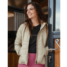 Woman wearing a beige puffer jacket and pink pants standing in front of a door.