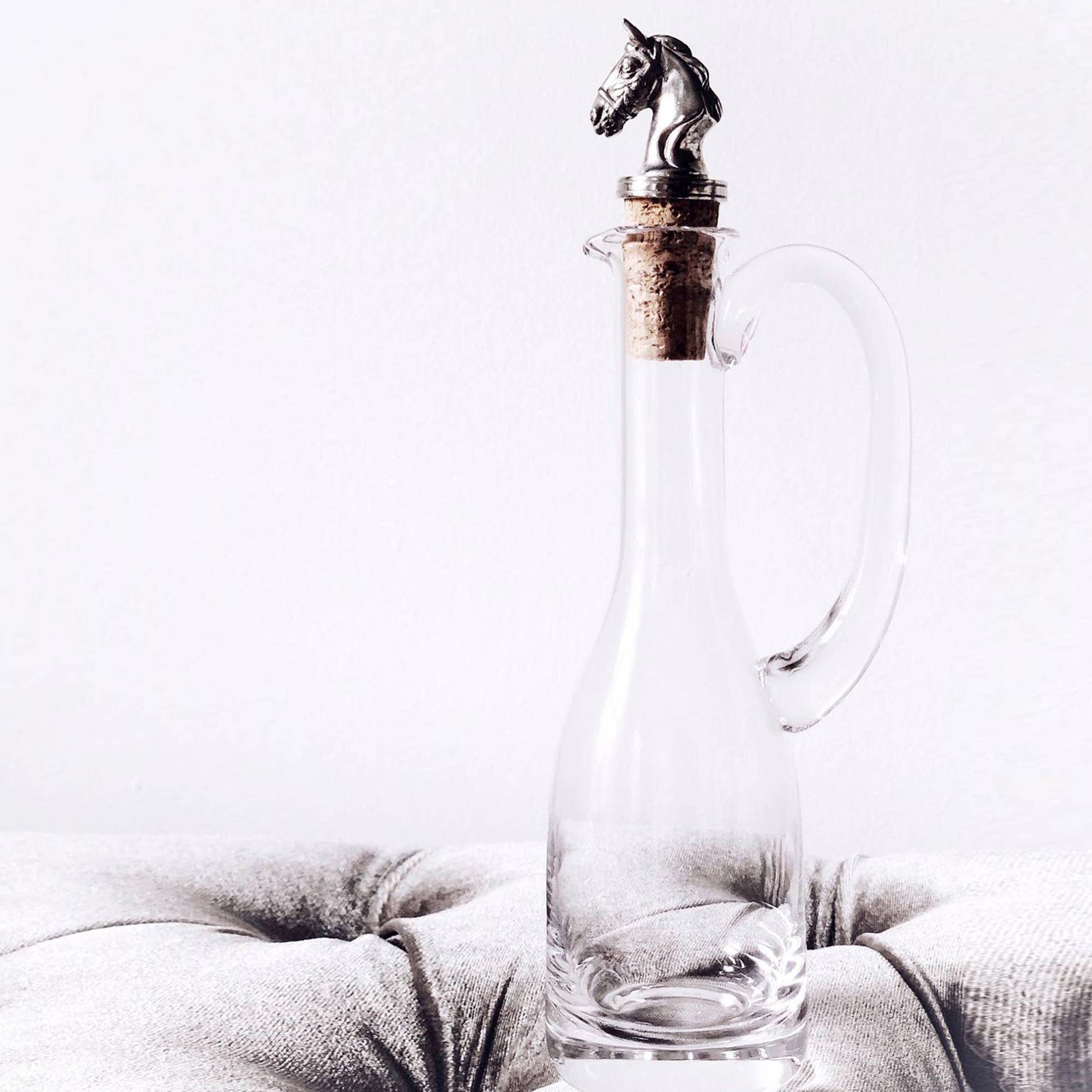 Glass decanter with horse head stopper on a light gray cushion