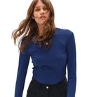 A woman wearing a fitted royal blue long-sleeve top with a small silver chest emblem, paired with black pants, against a plain white background.