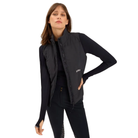 A woman modeling a black sleeveless zip-front puffer vest over a black long-sleeve top and black pants, photographed against a plain white studio background.
