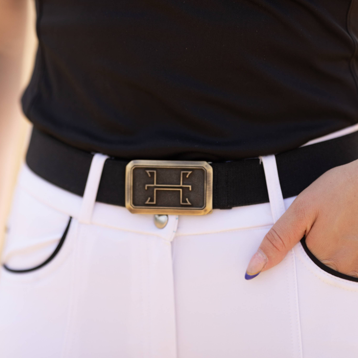Person wearing a black belt with a gold buckle on white pants.