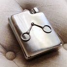 Silver flask with a decorative clip on a textured surface