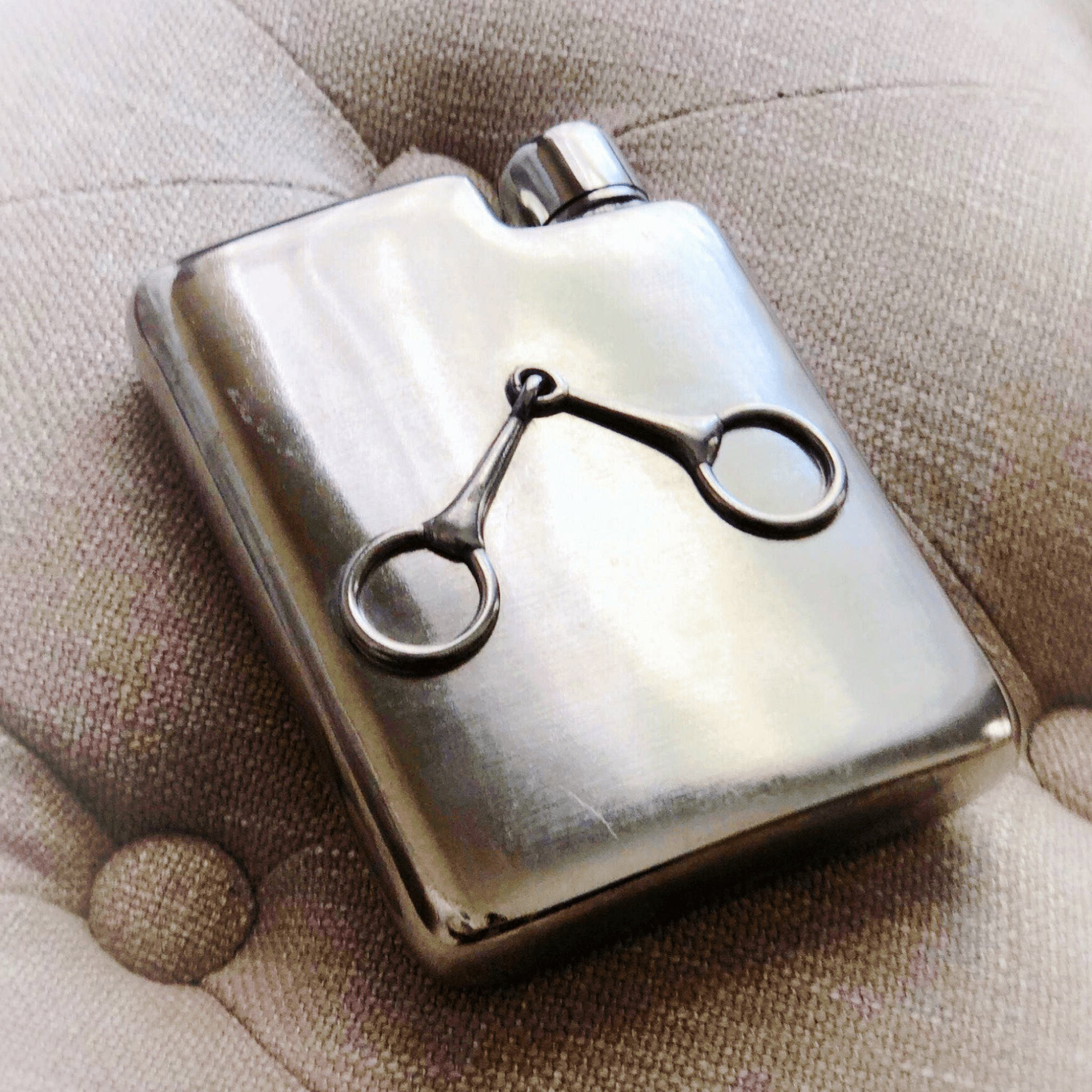 Silver flask with a decorative clip on a textured surface