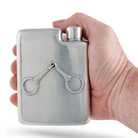 Hand holding a silver flask with equestrian stirrup design on a white background