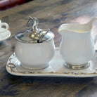 White ceramic sugar bowl and creamer set with silver horse finial on a wooden surface