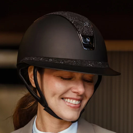 Person wearing a black riding helmet and beige equestrian jacket.