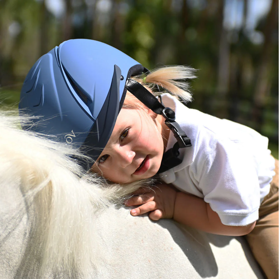 Child wearing a blue riding helmet on a horse with a blurred natural background