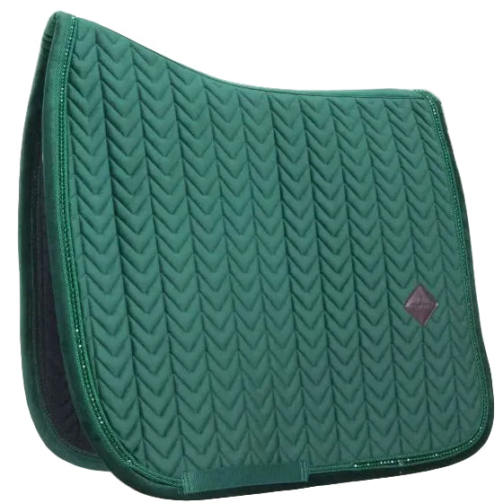 A dark teal green quilted equestrian saddle pad with a chevron pattern and a small diamond-shaped logo patch on the right side, set against a plain off-white background.