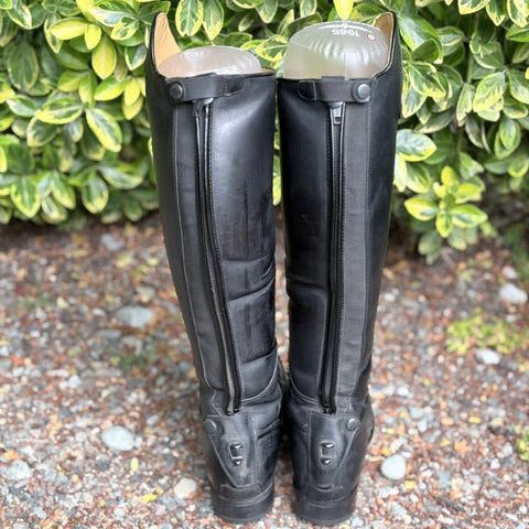 A pair of tall black leather riding boots facing backwards.