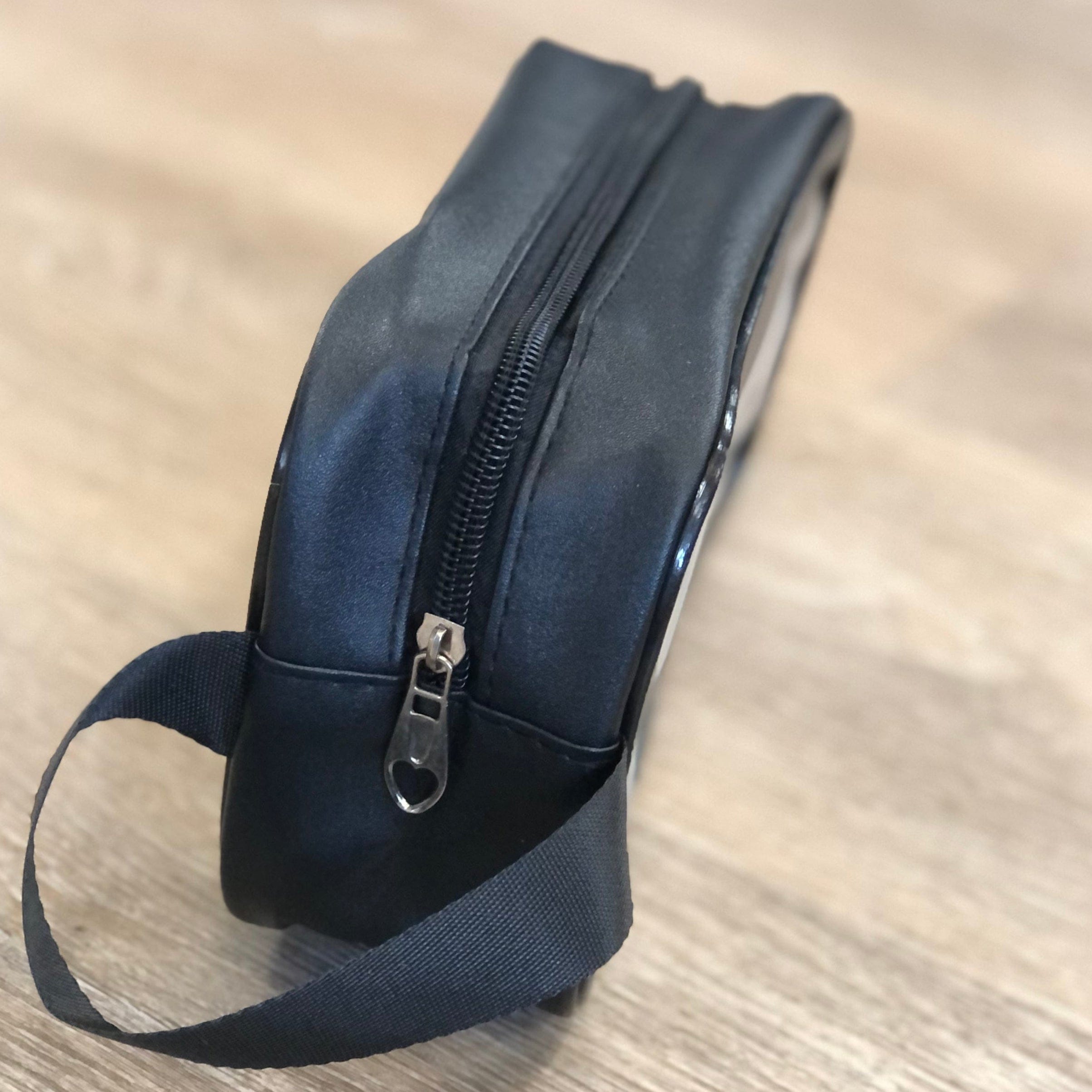 Black leather pouch with a strap on a wooden surface