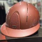 A metallic pink horse riding helmet displayed on a black box inside a store.