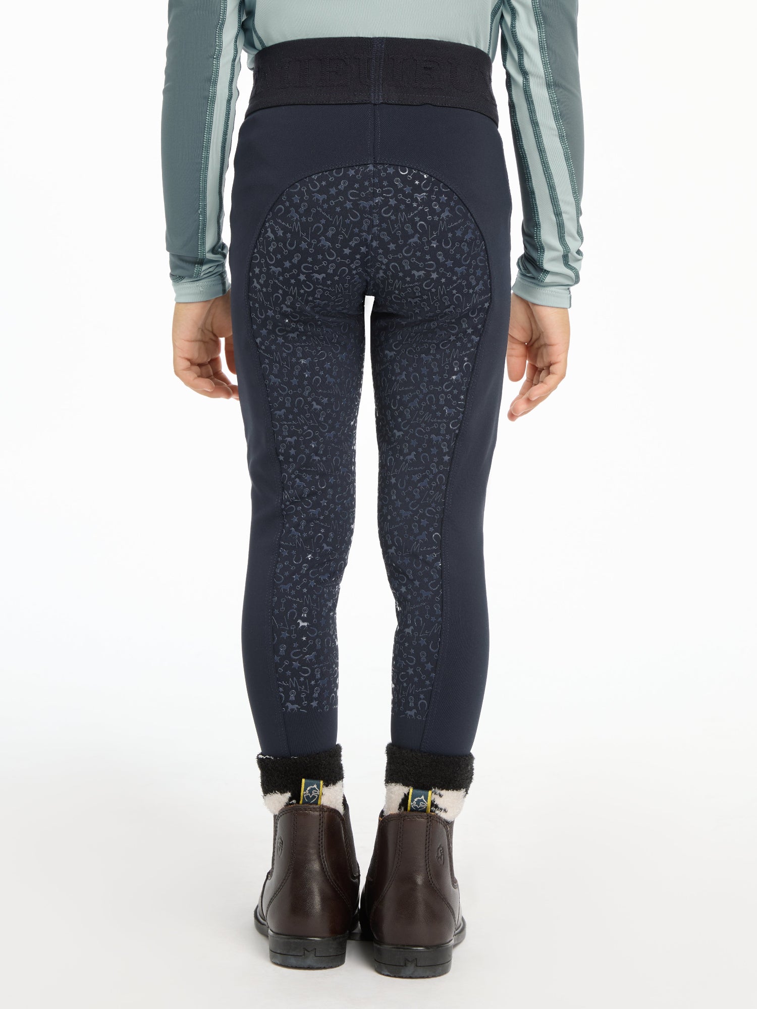 Rear view of a person wearing dark navy leggings with a subtle speckled pattern, a gray long-sleeve top, and dark brown ankle boots against a plain white background.