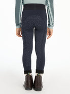 Rear view of a person wearing dark navy leggings with a subtle speckled pattern, a gray long-sleeve top, and dark brown ankle boots against a plain white background.