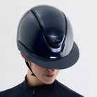 Person wearing a black equestrian helmet and outfit on a light gray background
