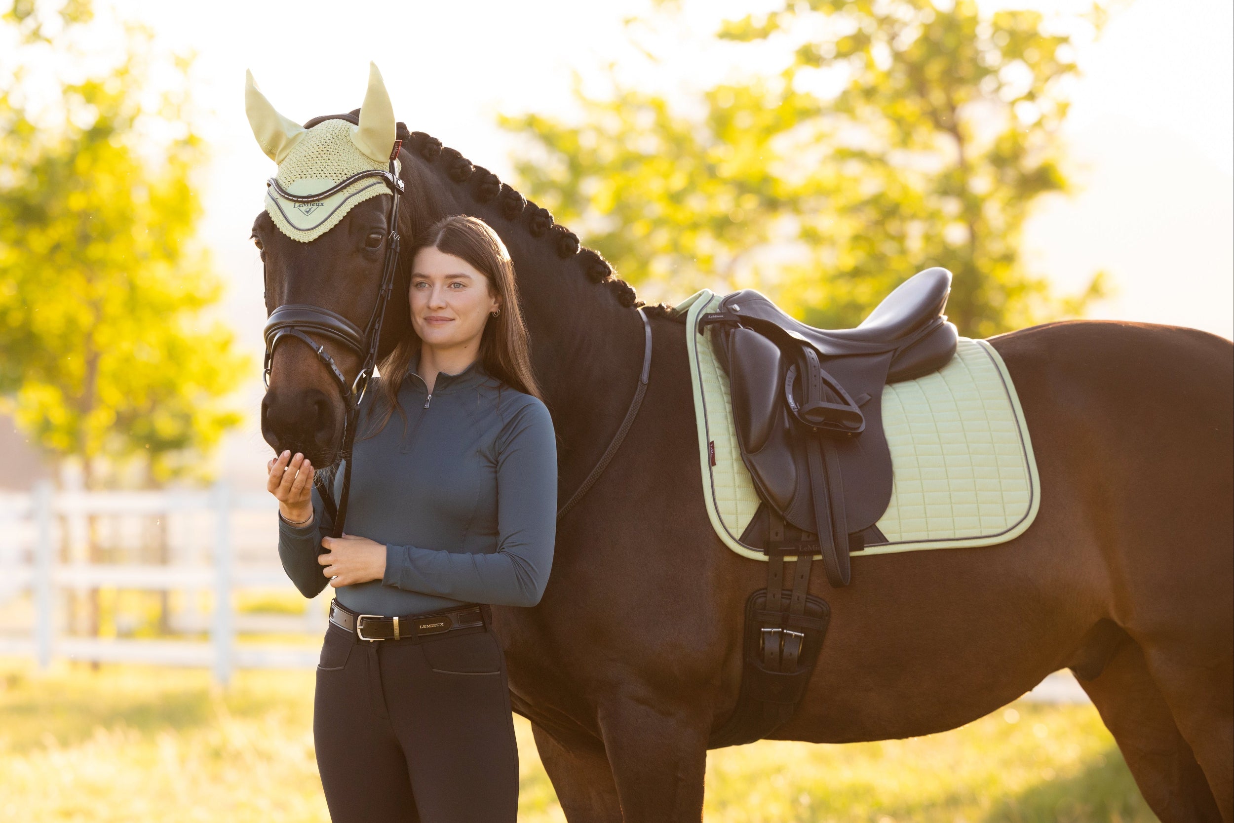 Woman standing next to a horse in an outdoor setting with trees and grass.