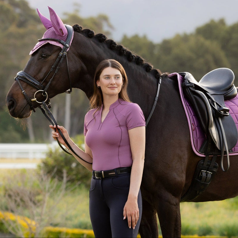 Woman standing next to a horse with a purple saddle pad in an outdoor setting