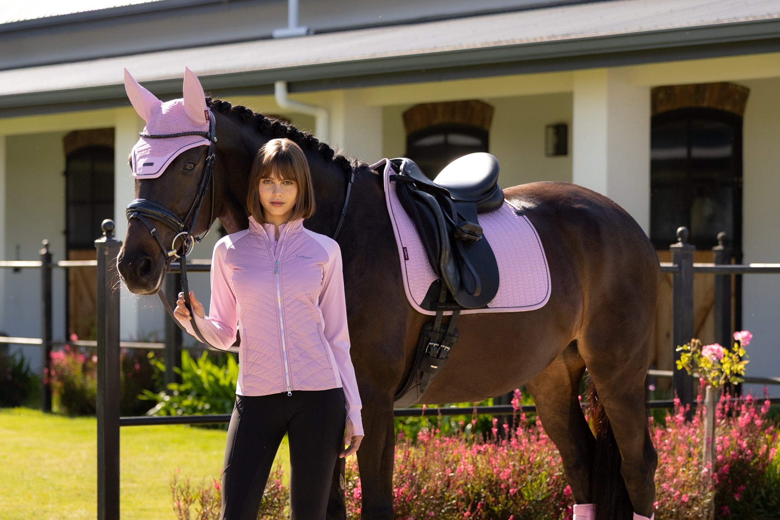 Woman in equestrian attire standing next to a horse with pink leg wraps in an outdoor setting.