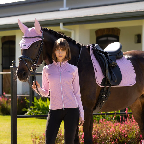 Woman in equestrian attire standing next to a horse with pink leg wraps in an outdoor setting.