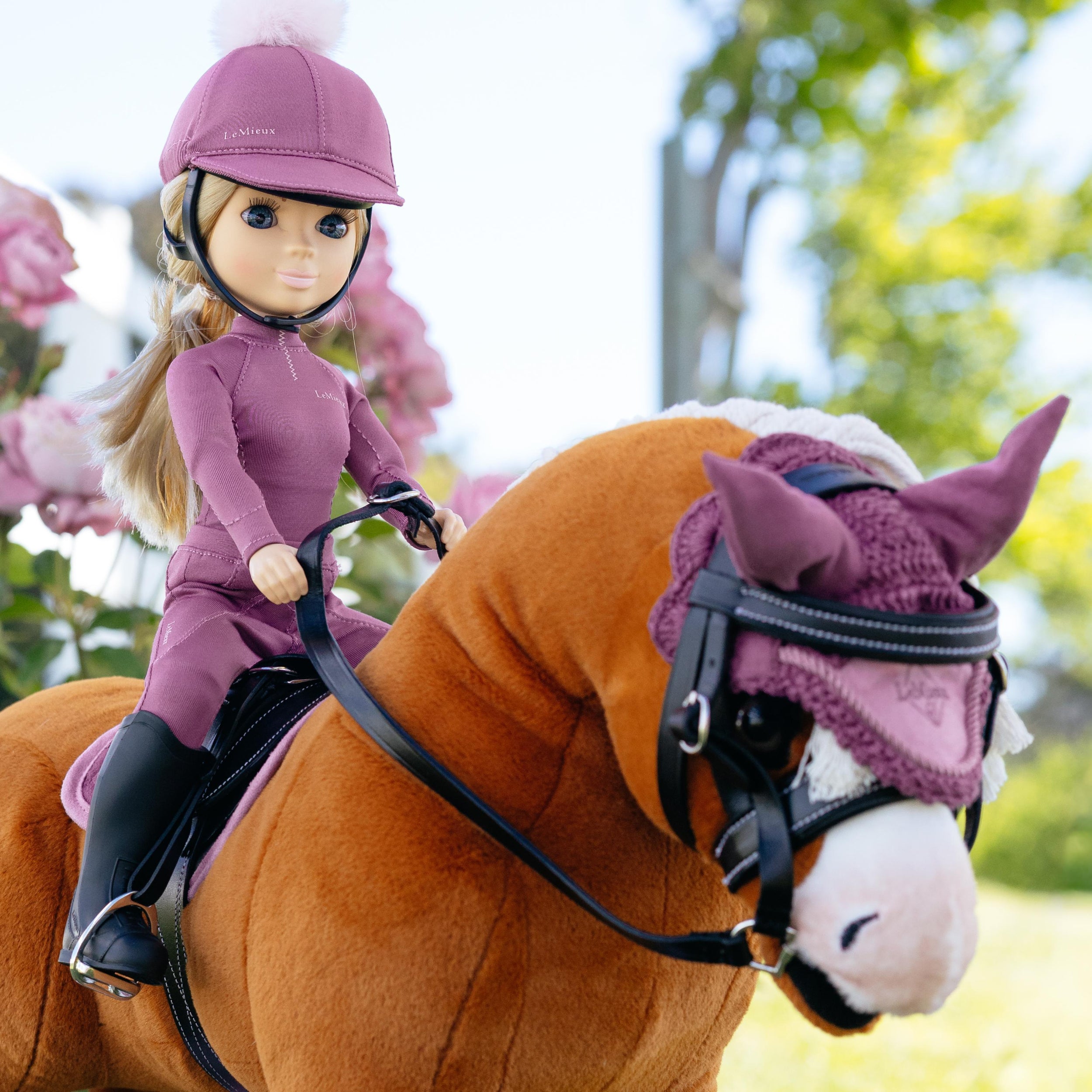 Doll in equestrian gear riding a toy horse with a pink bridle.