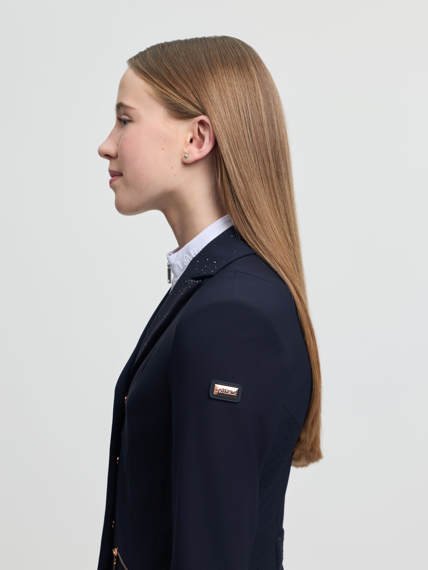 Woman wearing a navy blazer with a brand logo on a light gray background
