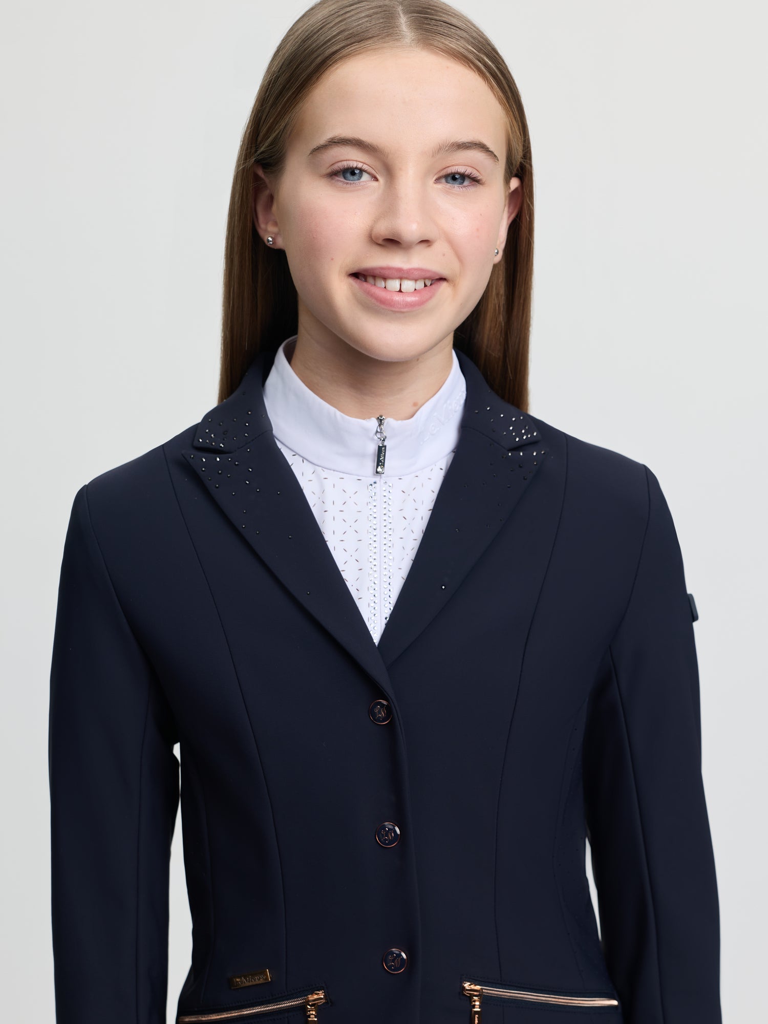 Girl wearing a navy blue equestrian jacket on a light gray background