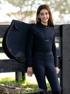 Person wearing equestrian attire next to a saddle pad outdoors
