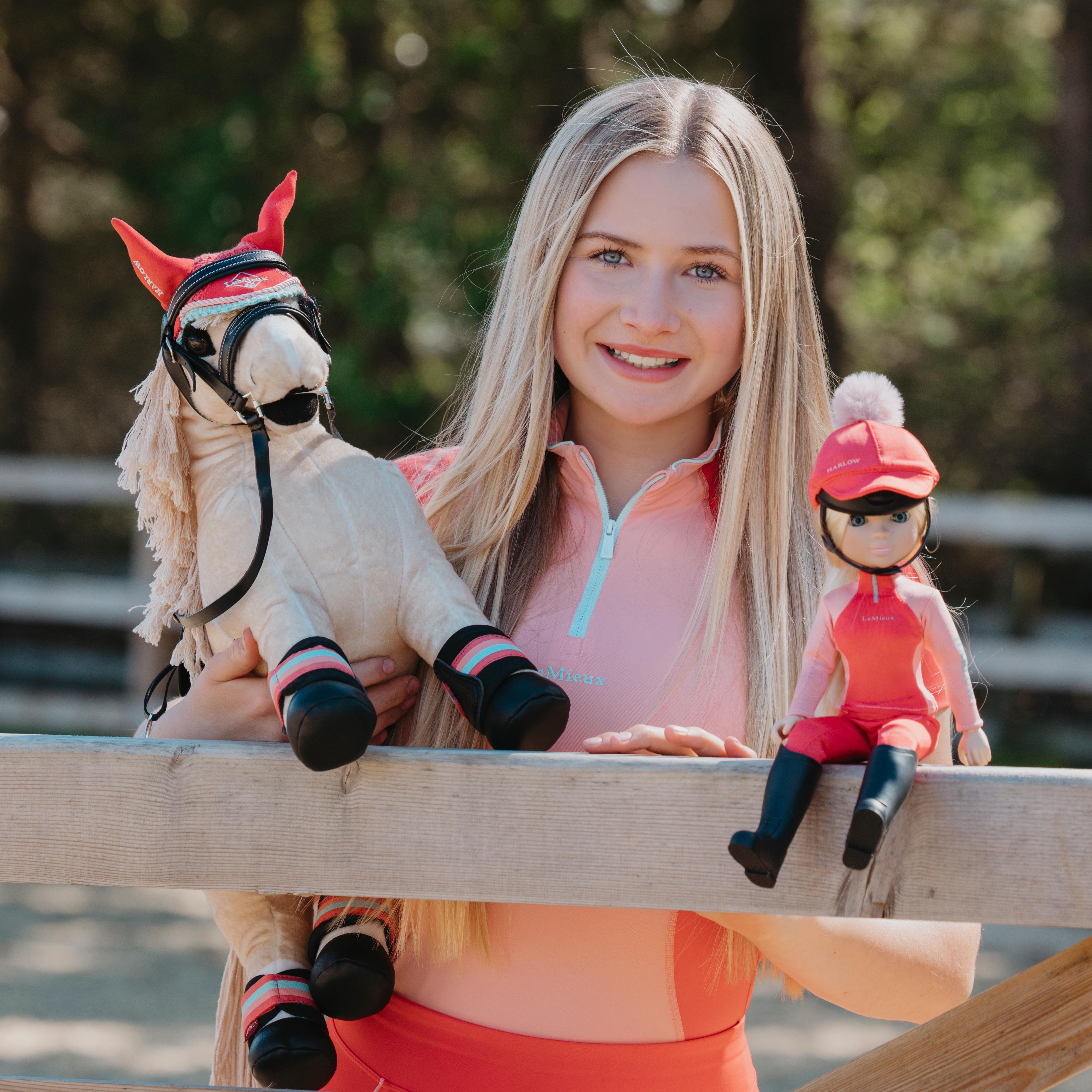 Young girl holding a toy horse and a doll with a helmet outdoors.