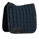 A LeMieux equestrian saddle pad in navy blue with a quilted grid pattern, featuring a black leather pad at the front and white piping along the edges, shown against a light gray background.